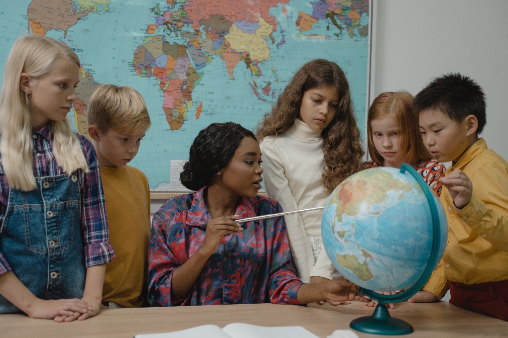 a teacher with students pointing to a globe