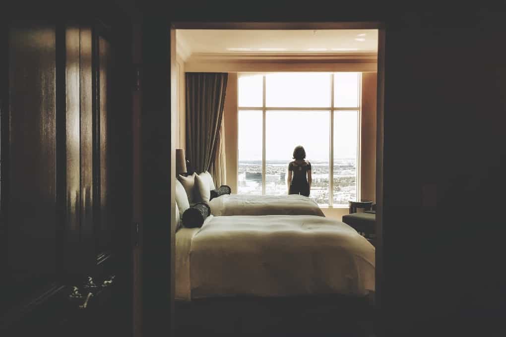 woman in hotel room looking out window at the sky