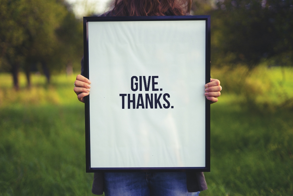 woman holding a sign that says "give thanks"